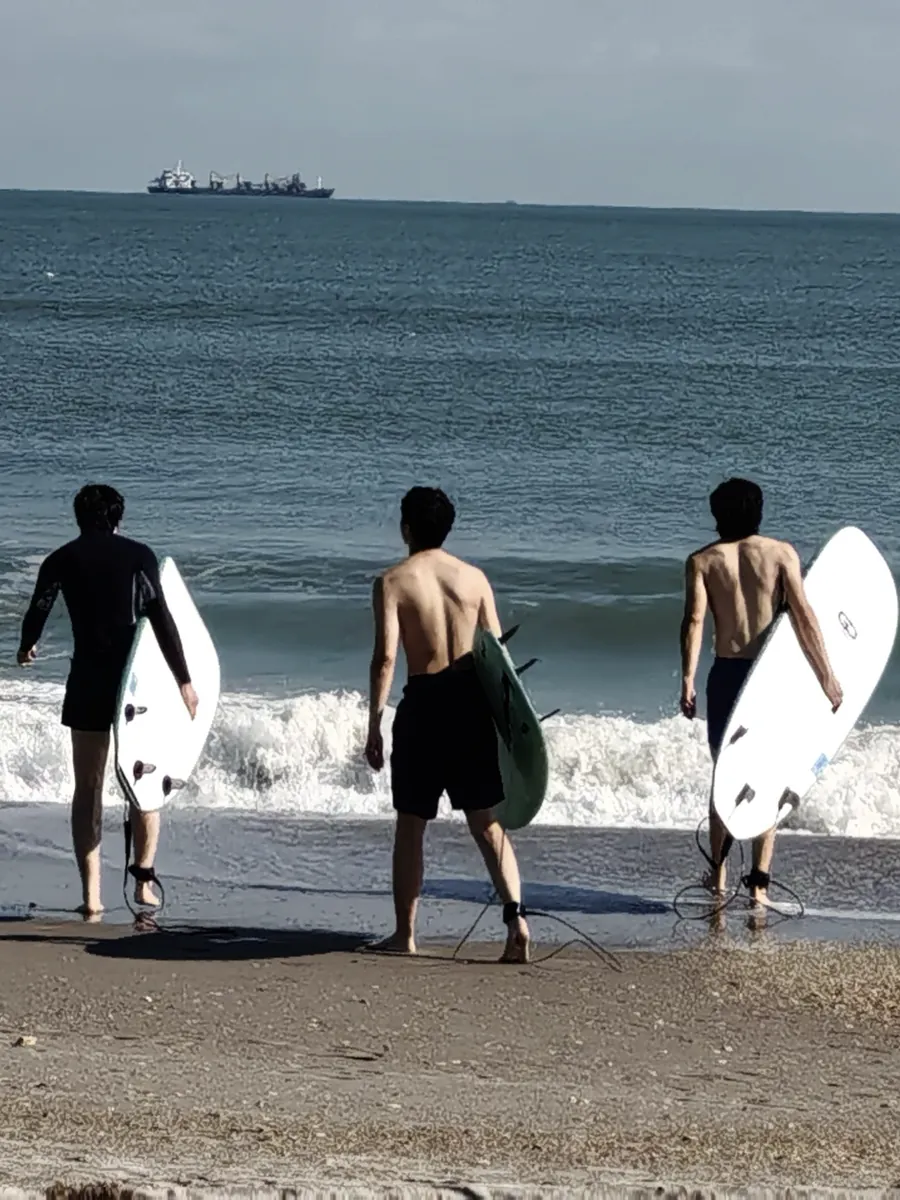 三名冲浪者从海岸走向浪线